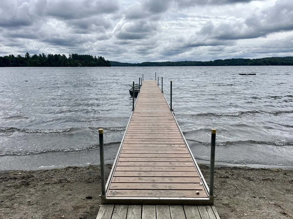 A wooden dock extending over Caspian Lake, Greensboro Vermont, under a cloudy sky